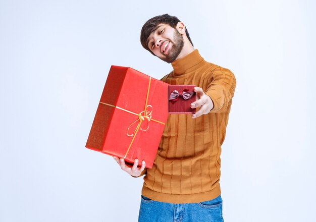 Homme tenant des coffrets cadeaux rouges grands et petits et offrant l'un d'eux à sa petite amie.