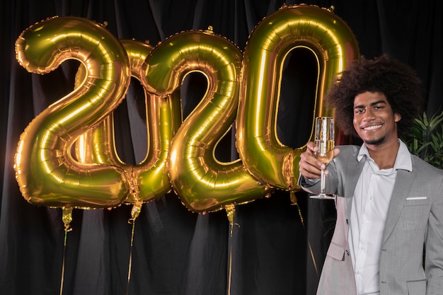 Homme tenant une coupe de champagne et bonne année 2020 ballons