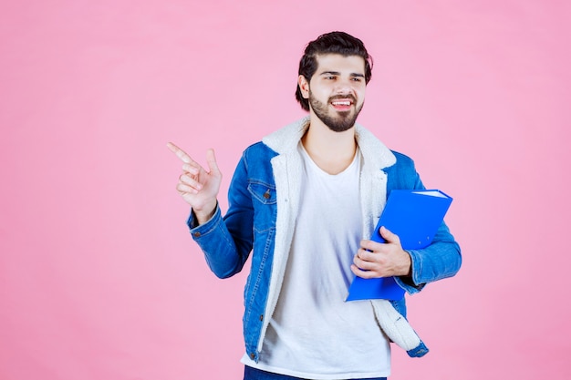 Homme tenant un dossier bleu et pointant vers le côté gauche