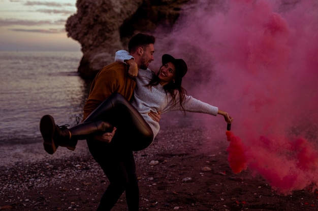 Homme tenant une femme dans les bras avec une bombe de fumée rose