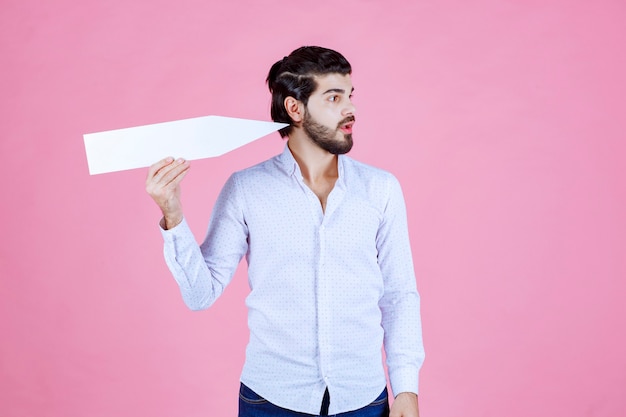 Homme tenant une flèche blanche et montrant le côté est.