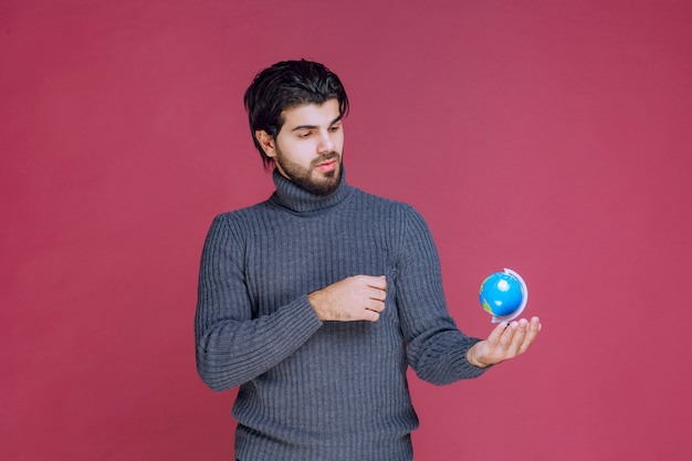 Homme tenant un mini globe bleu et en le regardant attentivement.
