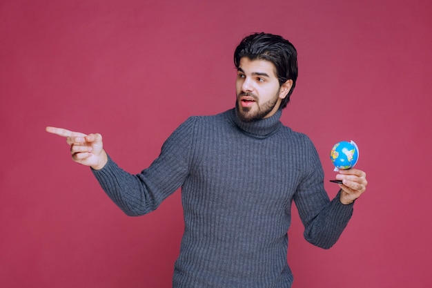 Homme tenant un mini globe et pointant vers la gauche.