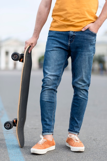 Homme tenant une planche à roulettes et une main dans la poche