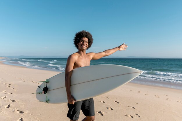 Homme tenant une planche de surf et pointant en mer