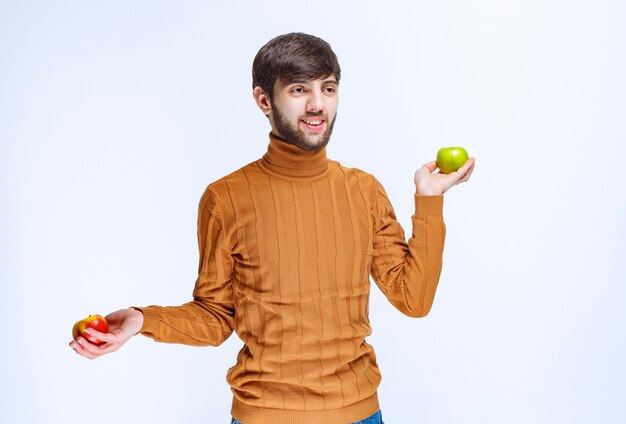 Homme tenant des pommes rouges et vertes dans les deux mains.