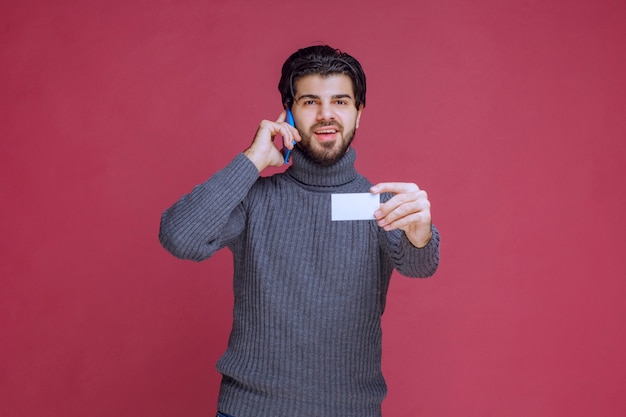 Homme tenant sa carte de visite et appelant le numéro de contact dessus.