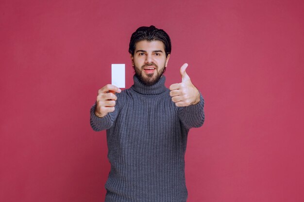 Homme tenant sa carte de visite et fait signe de la main positive.