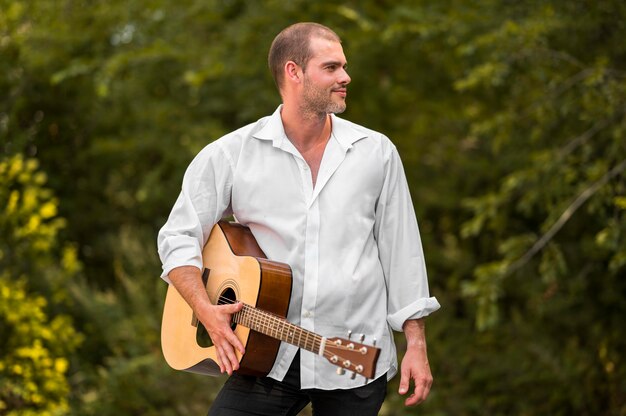 Homme tenant sa guitare dans la nature