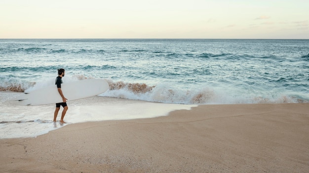 Homme tenant sa planche de surf long shot