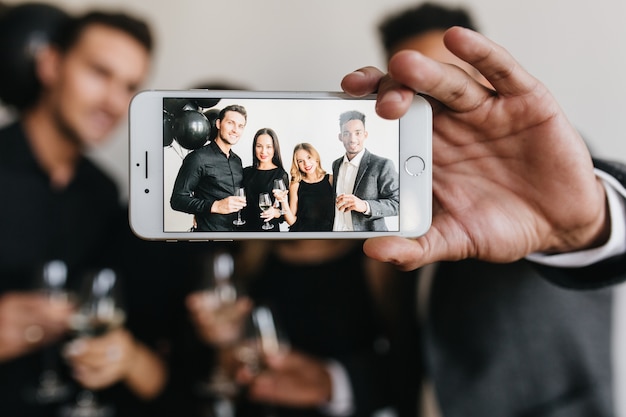 Homme tenant un smartphone blanc avec photo de jeunes avec des lunettes à l'écran