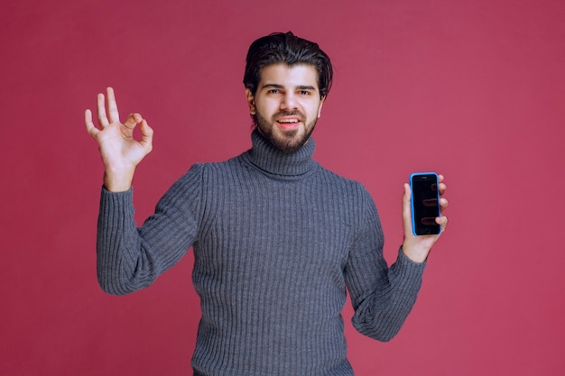 Homme tenant un smartphone et faisant un bon signe de la main.
