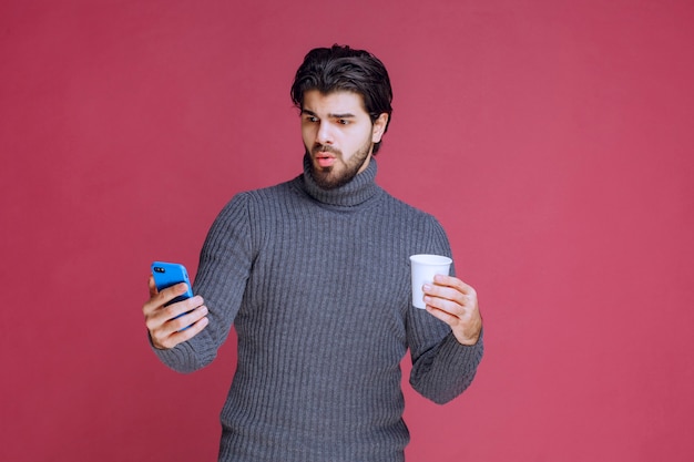 Homme tenant un smartphone et une tasse de café et semble confus.