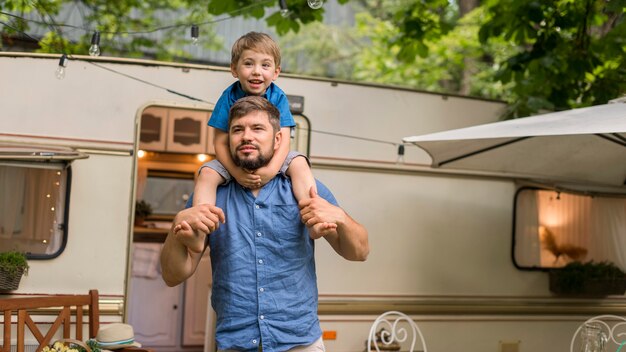 Homme tenant son fils sur ses épaules à côté d'une caravane avec copie espace