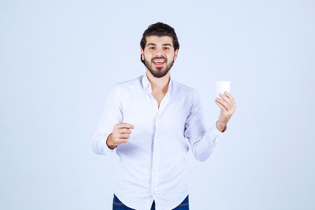 Homme tenant une tasse de café dans une main et présentant sa carte de visite dans une autre main