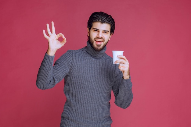 Homme tenant une tasse de café jetable et fait signe de plaisir.