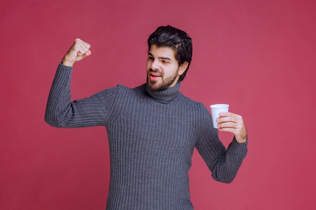 Homme tenant une tasse à café jetable, se sentant puissant et énergique.