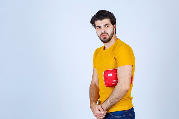 Homme tenant une trousse de premiers soins rouge sous le bras.