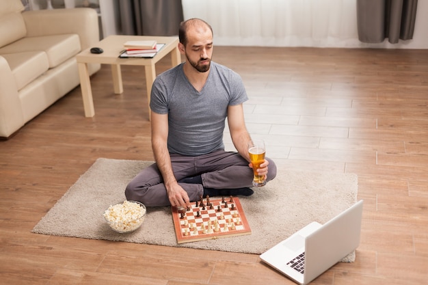 Homme tenant un verre à bière tout en jouant aux échecs en ligne pendant l'auto-isolement.