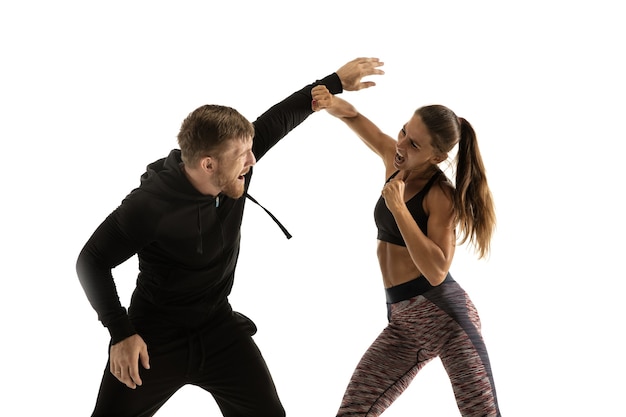 Homme en tenue noire et femme athlétique se battre sur le mur blanc du studio