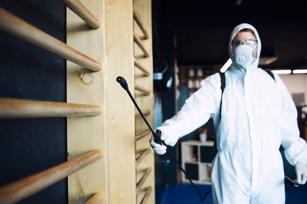 Homme en tenue de protection blanche désinfectant et équipement de fitness et poids pour arrêter la propagation du virus corona très contagieux