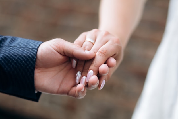 L'homme tient la main d'une femme avec une manucure rose tendre à l'extérieur