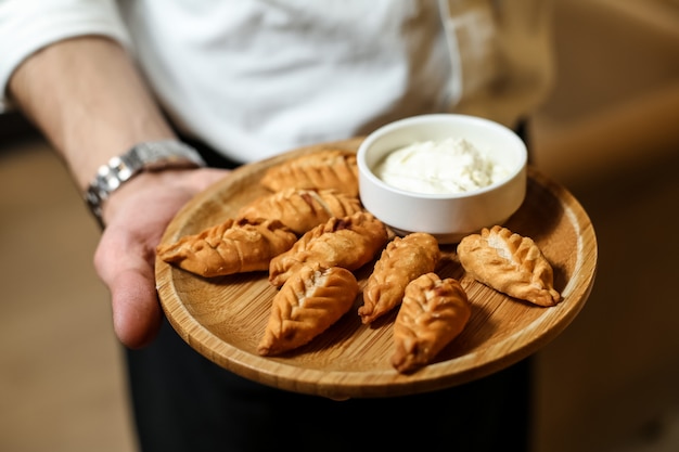 L'homme tient un plat traditionnel gurza frit sur les boulettes de planche de bois avec de la viande hachée sumakh vue côté crème sure