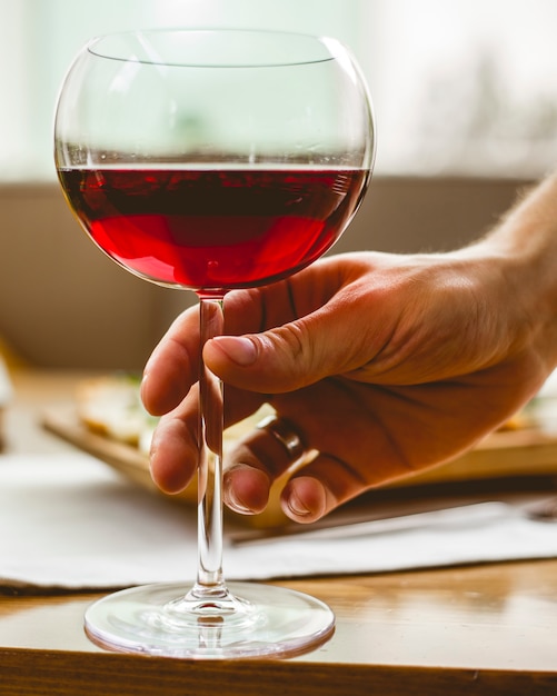 L'homme tient le verre avec une vue latérale du vin rouge