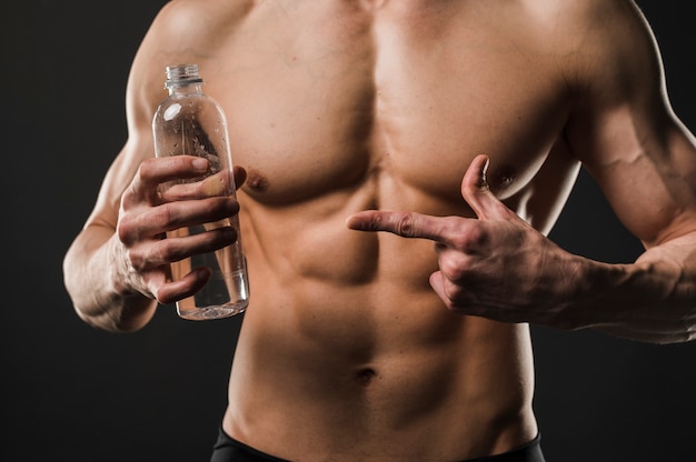 Homme torse nu athlétique pointant sur une bouteille d'eau
