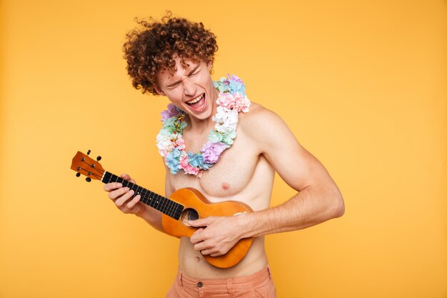 Homme torse nu séduisant dans des vêtements d'été jouant du ukulélé