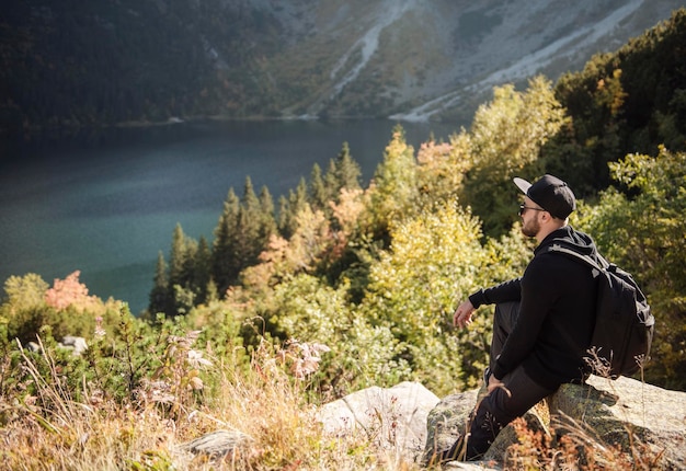 Homme touriste se reposant au sommet d'une colline, regardant de magnifiques paysages de montagnes et de lac.