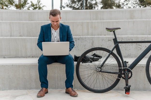 Photo gratuite homme travaillant sur un ordinateur portable à côté de son vélo à l'extérieur