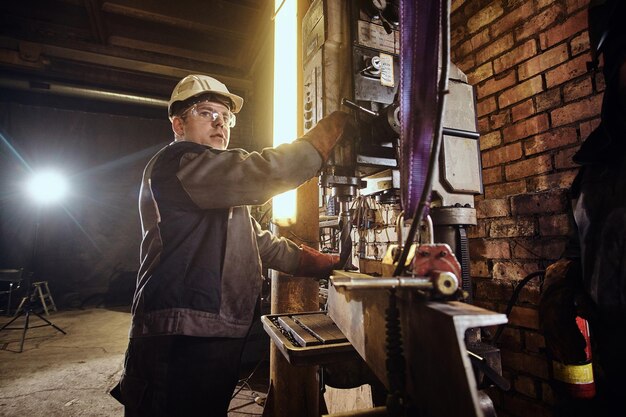 L'homme travaille avec une perceuse géante dans une usine de métal occupée.