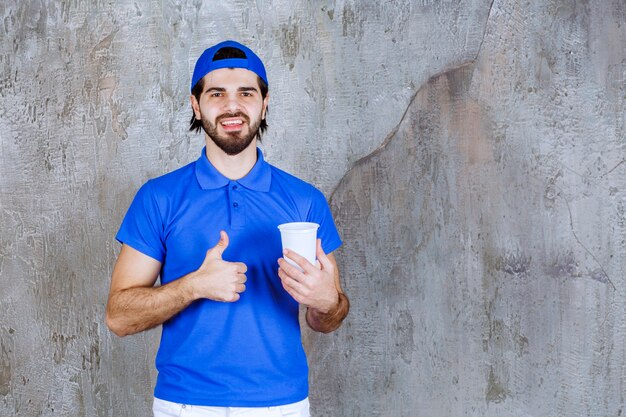 Homme en uniforme bleu tenant une boisson à emporter et montrant un signe positif de la main.