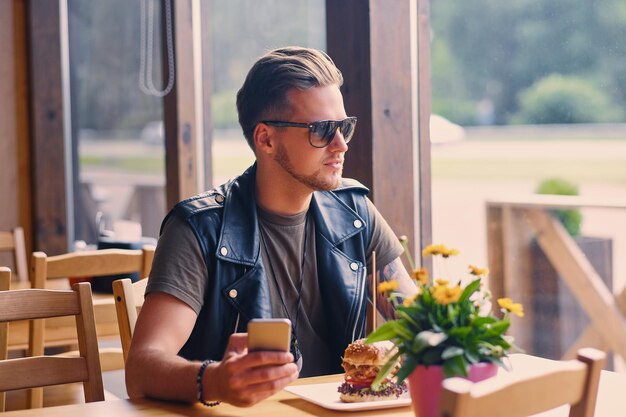 Homme urbain élégant vêtu d'une veste en cuir à l'aide d'un smartphone dans un café.