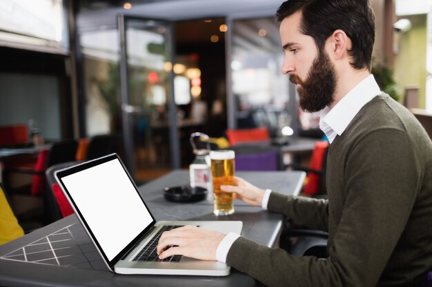 Homme utilisant un ordinateur portable tout en ayant un verre de bière