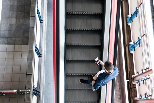 Homme utilisant un smartphone sur l&#39;escalator