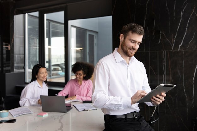 Homme utilisant une tablette pour travailler pendant que ses collègues féminines utilisent un ordinateur portable