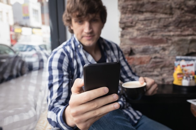 Homme utilisant un téléphone portable tout en prenant un café