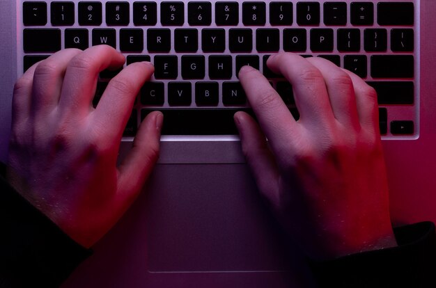 Un homme utilise un ordinateur portable closeup mains mâles en vue de dessus d'éclairage au néon