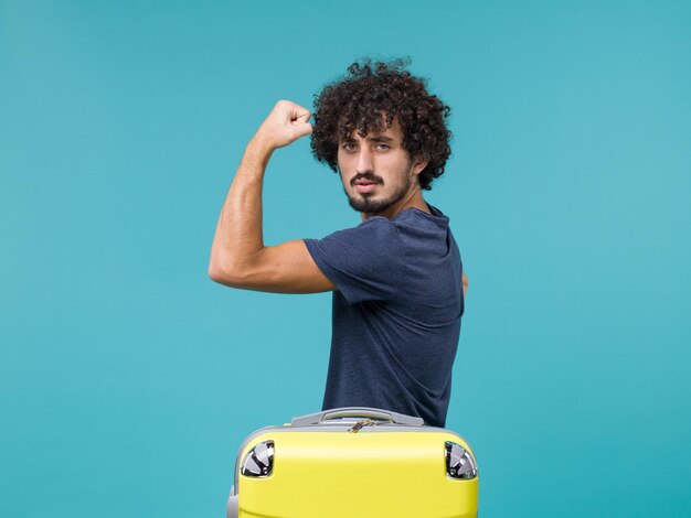 Photo gratuite homme en vacances fléchissant avec une valise jaune sur bleu