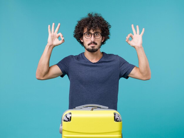 homme en vacances avec une grosse valise jaune sur bleu