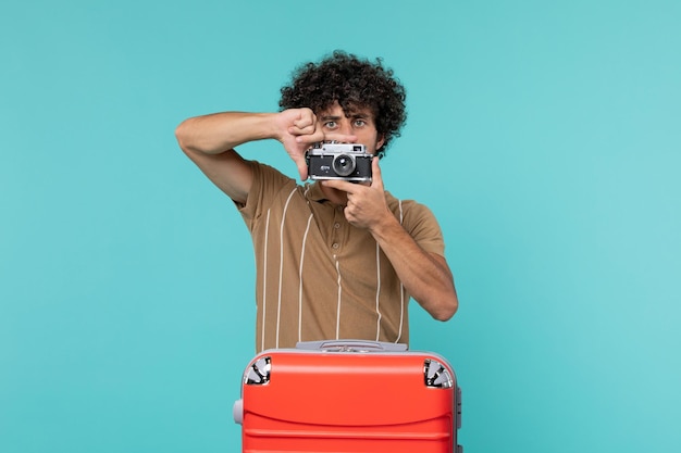 Photo gratuite homme en vacances avec une grosse valise rouge prenant des photos avec appareil photo sur bleu