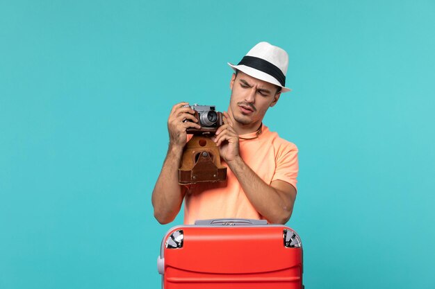 homme en vacances avec sa valise rouge prenant des photos avec appareil photo sur bleu