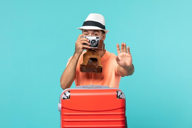 homme en vacances avec sa valise rouge prenant des photos avec appareil photo sur bleu