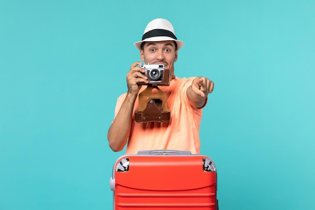 homme en vacances avec sa valise rouge prenant des photos avec appareil photo sur bleu