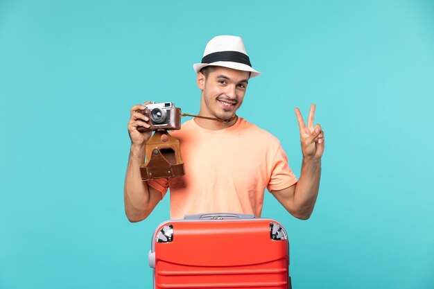 homme en vacances avec sa valise rouge prenant des photos avec appareil photo sur bleu