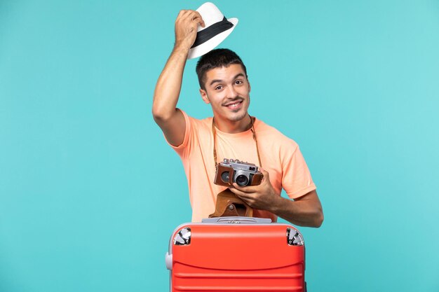 homme en vacances avec sa valise rouge et son appareil photo sur bleu