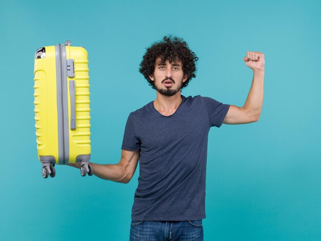 homme en vacances tenant une grosse valise jaune sur bleu