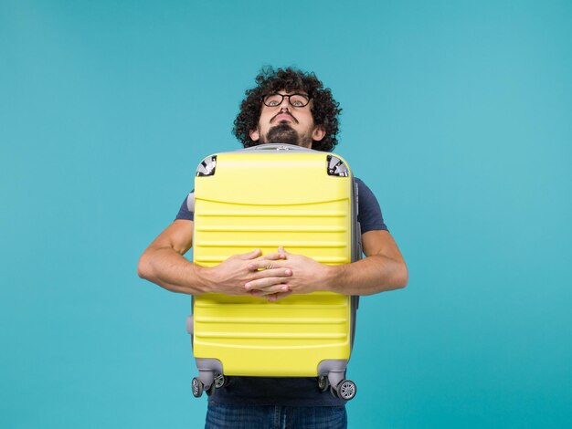 homme en vacances tenant une grosse valise jaune sur bleu